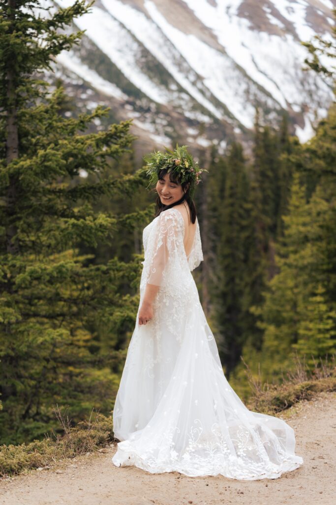 an adventurous bride in a lace wedding gown standing in front of mountains in canada