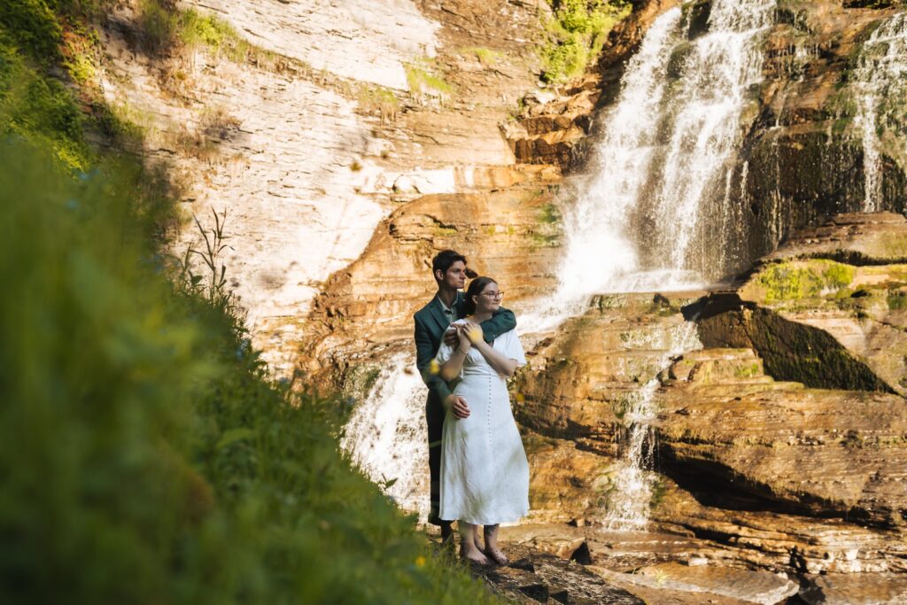 newlyweds that have just eloped hugging each other in front of a waterfall at Robert H. Treman State Park