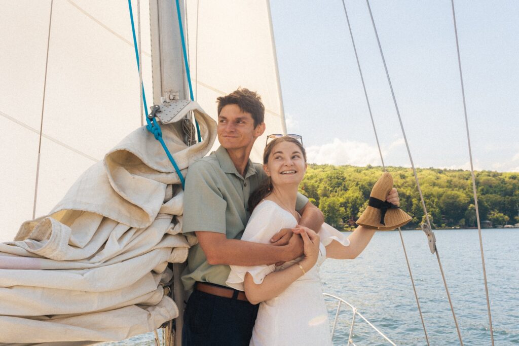 a newlywed couple that just eloped holds each other on a sailboat on Cayuga Lake in the finger lake region of new york