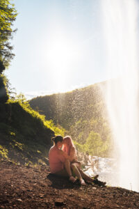 A woman sits in a man's lap under the Kaaterskill Falls in the catskills new york