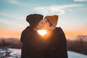 two women kissing on top of a mountain during sunset in the winter