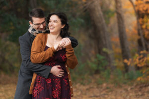 a man hugs a woman from behind in a forest