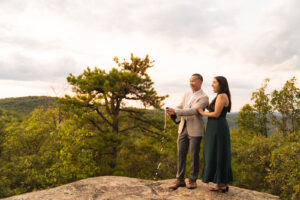 a man and woman pop champagne on the summit of a hiking trail 