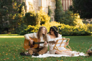 a man plays guitar and a woman paints on the lawn of a castle