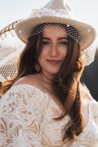 boho bride with a bridal western hat and veil smiles wearing a lace wedding gown on her elopement day