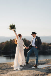 A newlywed couple that had just eloped at Minnewaska State Park Preserve celebrates. the boho bride raising her wildflower bouquet in her hand as the western cowboy groom admires her.