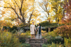 a woman and man stand together hand in hand wearing traditional Ondian attire in a garden