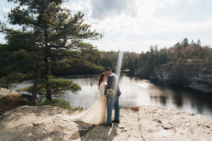 a bride and groom eloping on the cliffside of a lake