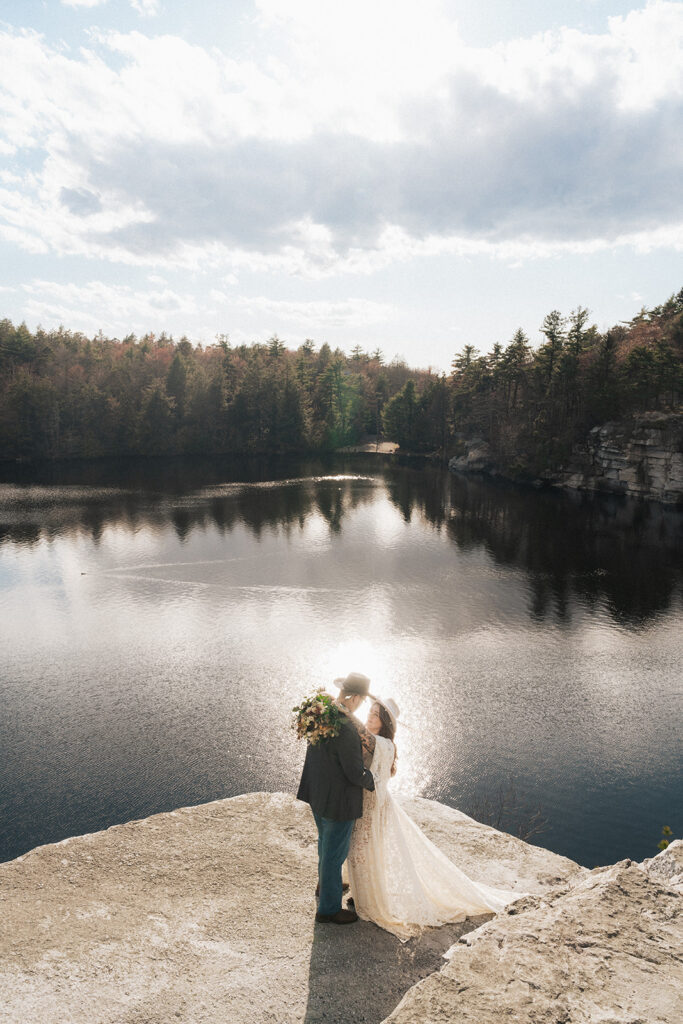 newlyweds embracing each other on the cliffside of a lake