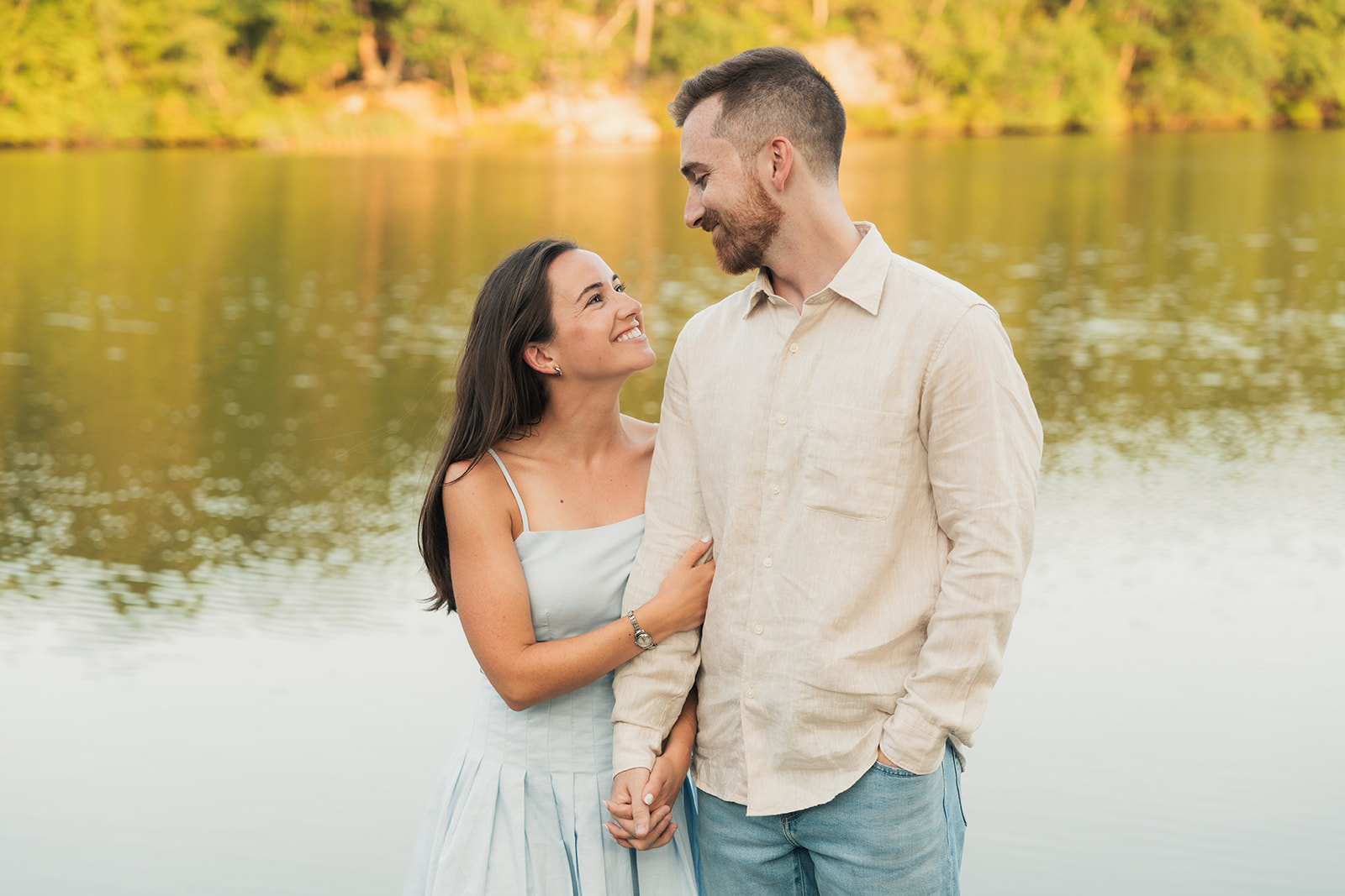 a newly engaged couple looks into each other's eyes during the summer with a lake in the background