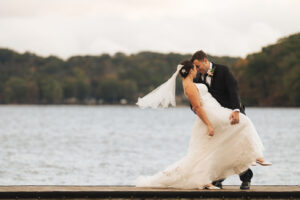 a groom dips his bride by a lake on their wedding day