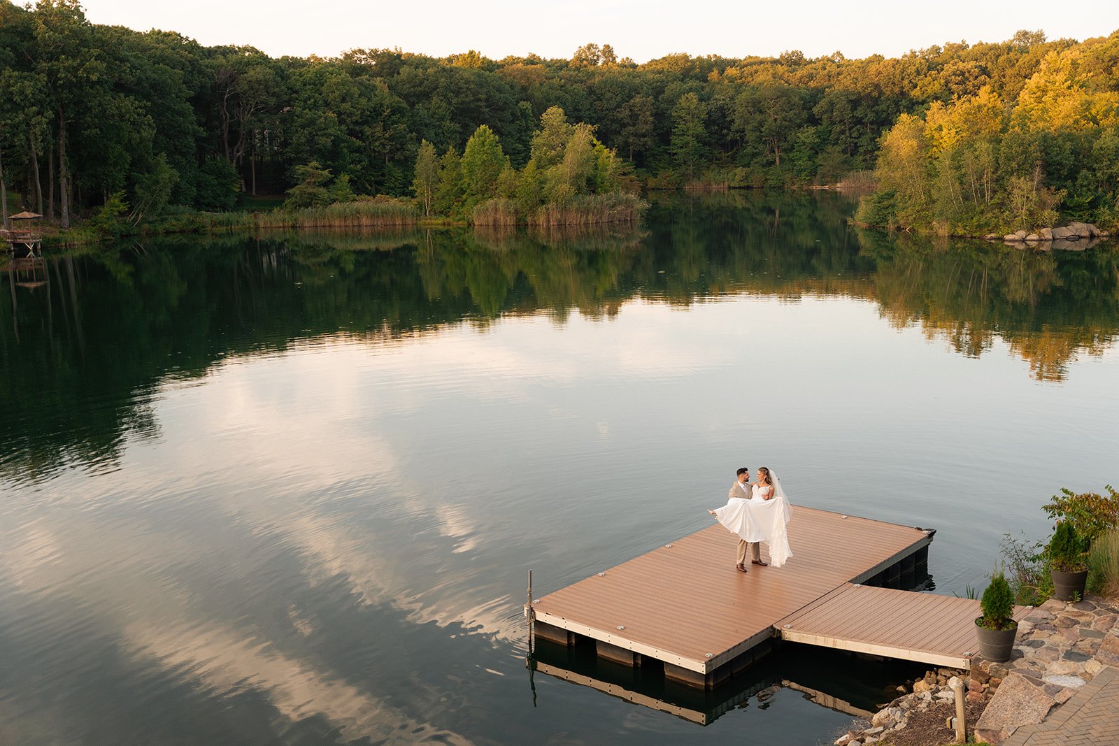 a groom picking up his bride on a dock overlooking a lake