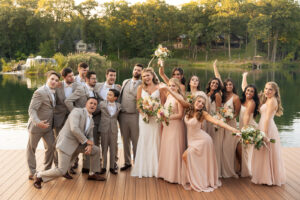 the groomsmen and bridal party strike fun poses with the newlyweds in the center on a dock overlooking a lake