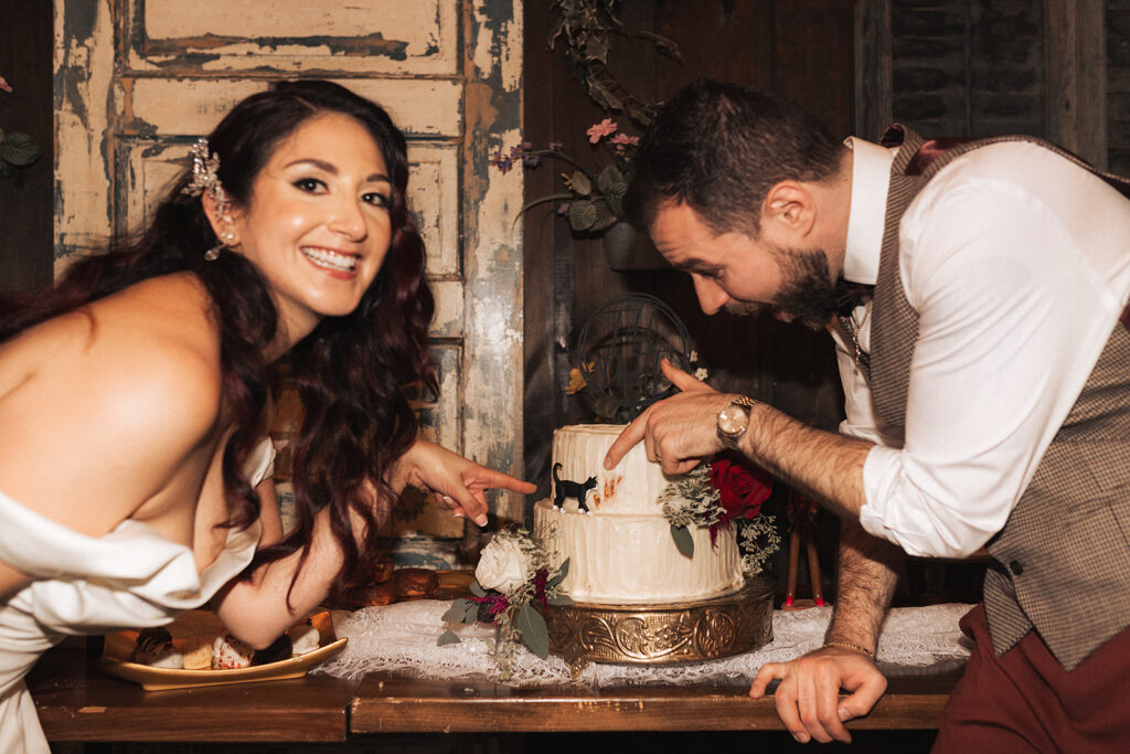 a bride and groom pointing to a cat statue on their wedding cake