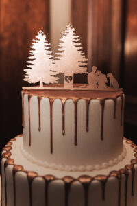 a wedding cake topper of two pine trees, a couple, and a dog