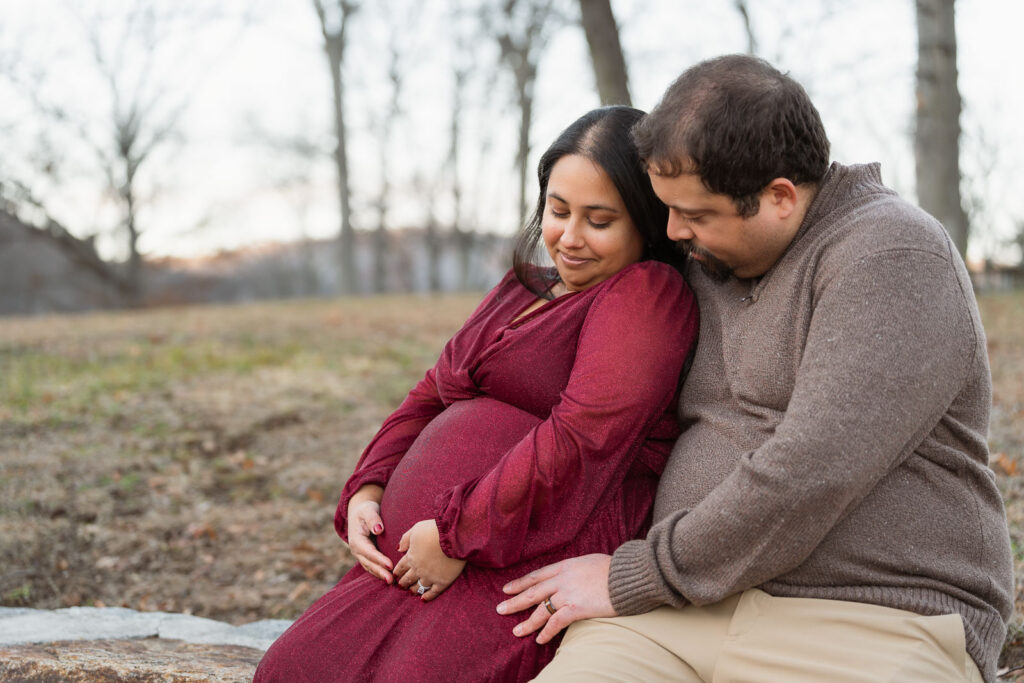 A winter maternity session at Bear Mountain State Park near Bear Mountain Inn, featuring golden hour light, a red dress, and a couple expecting their baby boy.