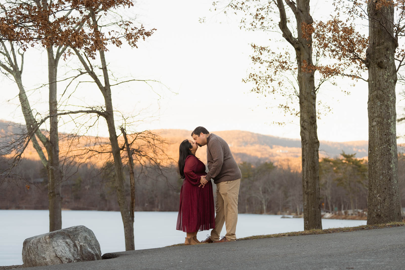 A winter maternity session at Bear Mountain State Park near Bear Mountain Inn, featuring golden hour light, a red dress, and a couple expecting their baby boy.