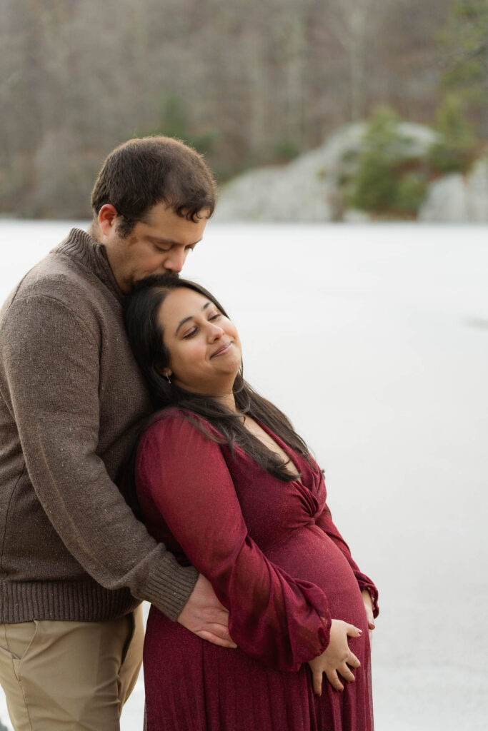 A winter maternity session at Bear Mountain State Park near Bear Mountain Inn, featuring golden hour light, a red dress, and a couple expecting their baby boy.