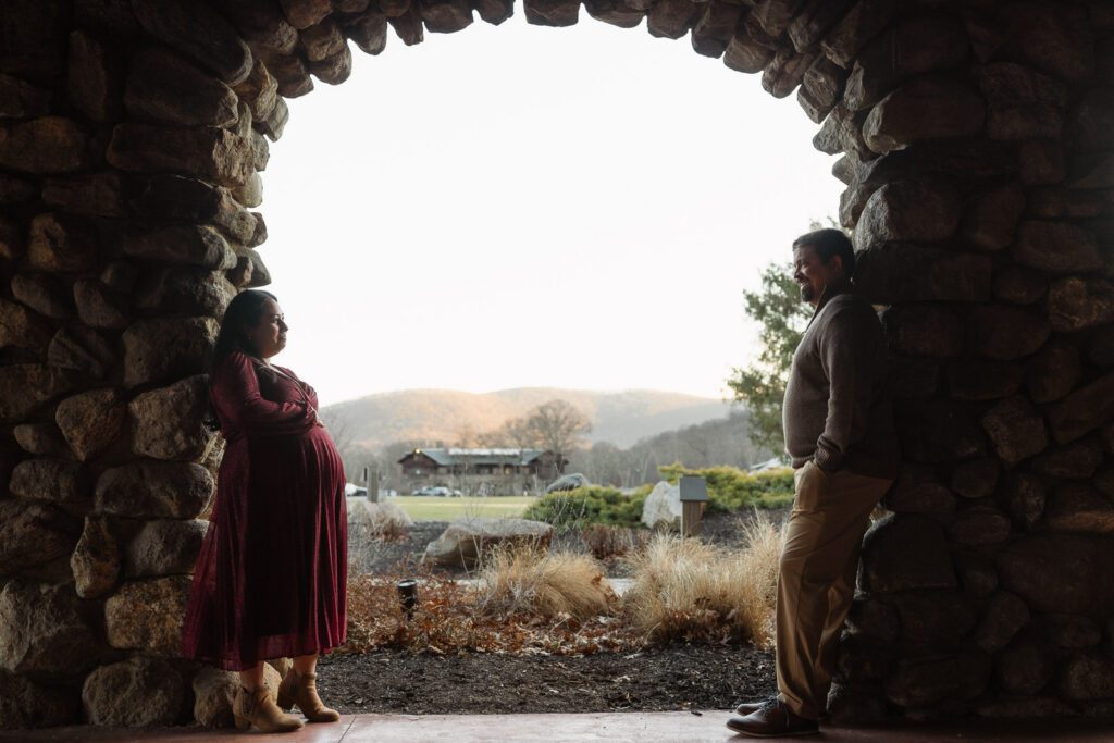 A winter maternity session at Bear Mountain State Park near Bear Mountain Inn, featuring golden hour light, a red dress, and a couple expecting their baby boy.