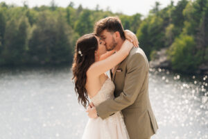 A couple that just got married kiss near a lake and forest in the Hudson Valley of New York.